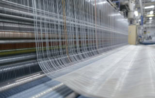 Close-up of synthetic yarn threads on a high-speed loom during textile warp sizing in a modern factory with industrial lighting.